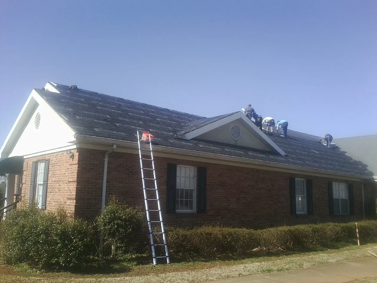 Crew tearing shingles off a brick ranch roof with a ladder set — Emergency Roof Repair work by our crew in Fort Bragg
