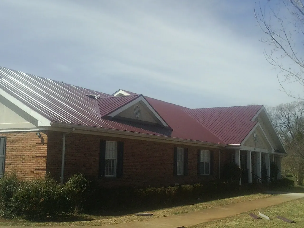 Red metal roof with gabled entries on a long brick building, from a Hail Damage Roof Repair job in Fort Bragg