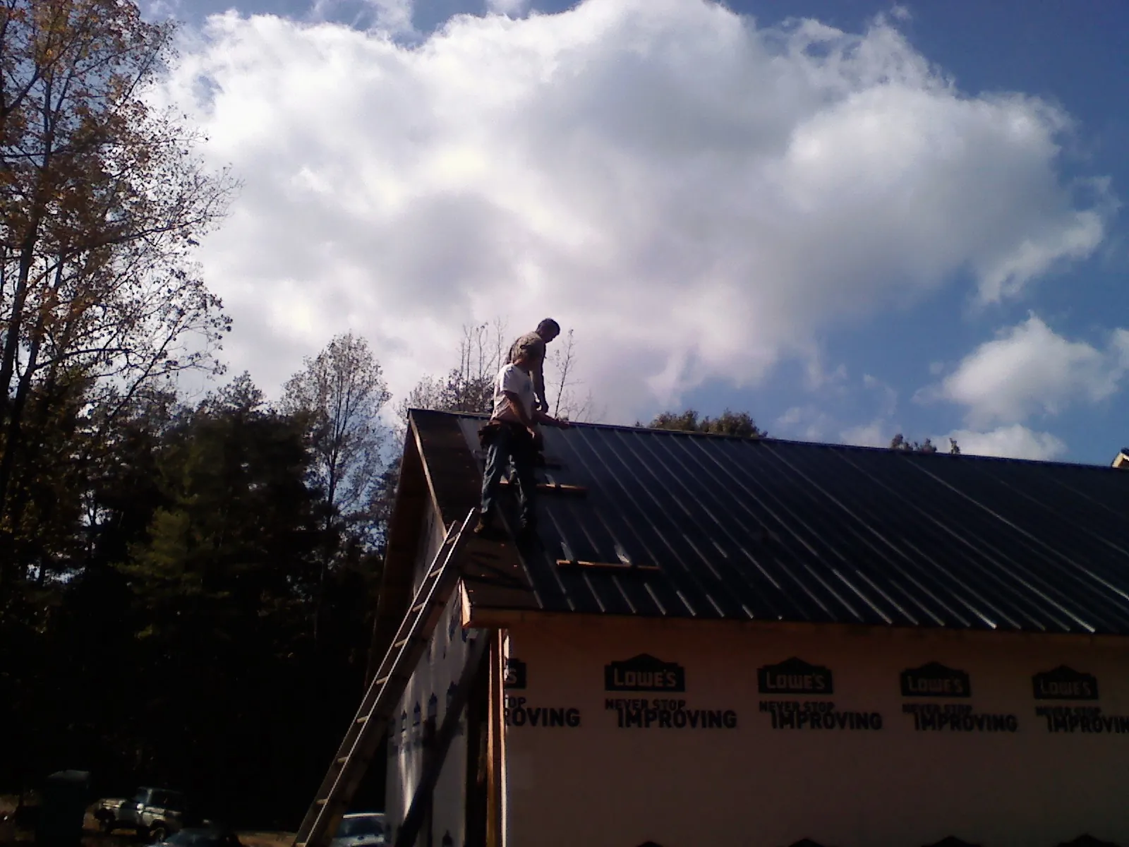 Roofer fastening dark metal panels high against a cloudy sky, from a Roof Inspection job in Fort Bragg