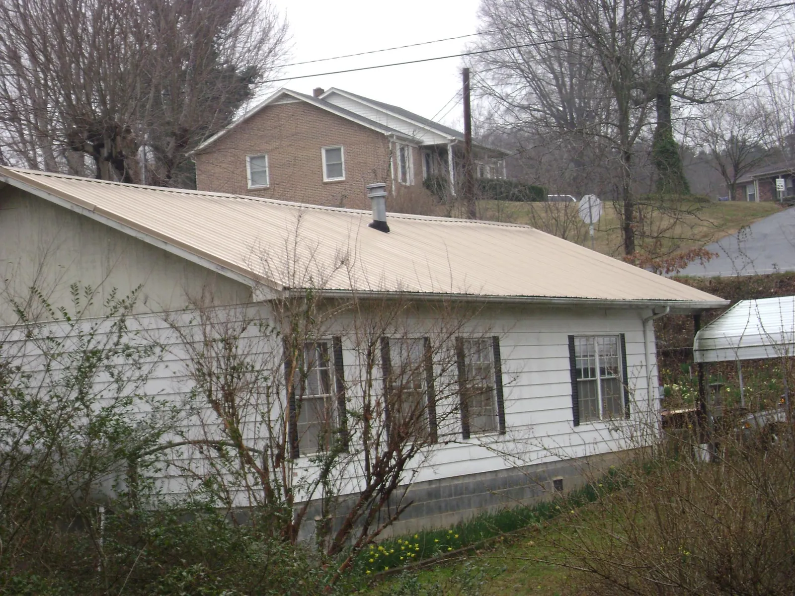 Tan metal roof on a white sided house set into a hillside — Commercial Roofing by Roofing Brothers in Fort Bragg